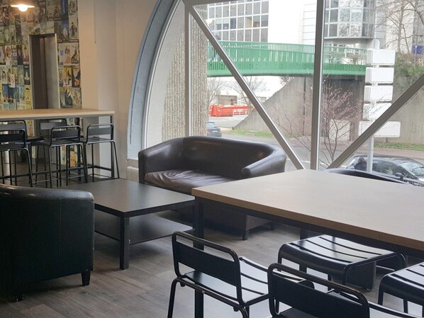 Un intérieur moderne avec une grande table, des chaises noires, un canapé en cuir et une vue sur un pont verdoyant à l’extérieur.