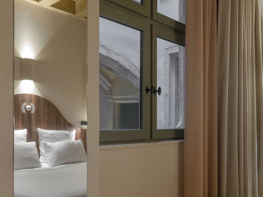 Un dormitorio con un ventanal grande, una cama y un espejo que refleja la habitación.