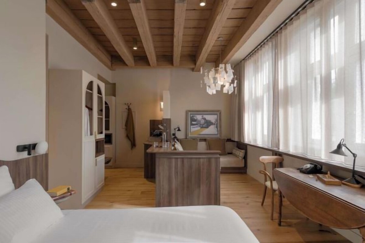 A modern hotel room with a wooden ceiling, a bed, a desk, and a small kitchenette.