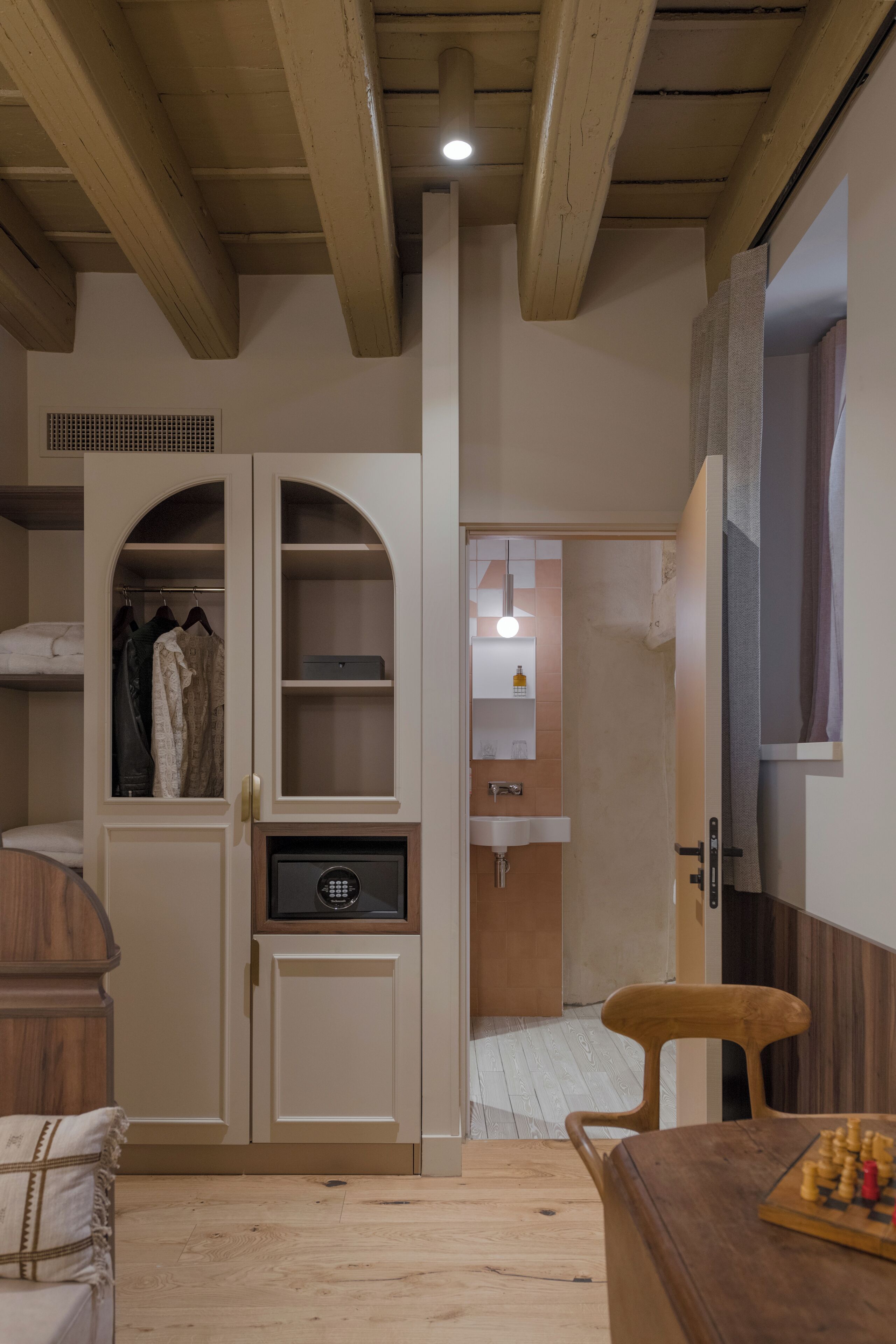 Una habitación con techo de madera, un armario con espejo, un lavabo y un tablero de ajedrez sobre una mesa.