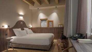 Quarto com cama grande, cabeceira de madeira, abajures, escrivaninha de madeira com telefone e livro, e quadros nas paredes.
