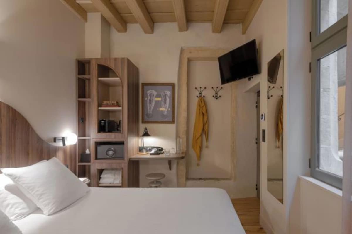 Un dormitorio con cama, armario de madera, escritorio con silla, televisor montado en la pared y ventana.