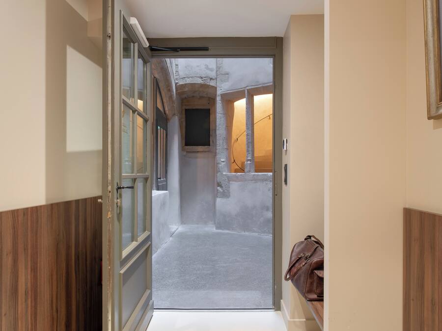 A narrow hallway with a wooden floor, a door leading to a room, and a framed certificate on the wall.