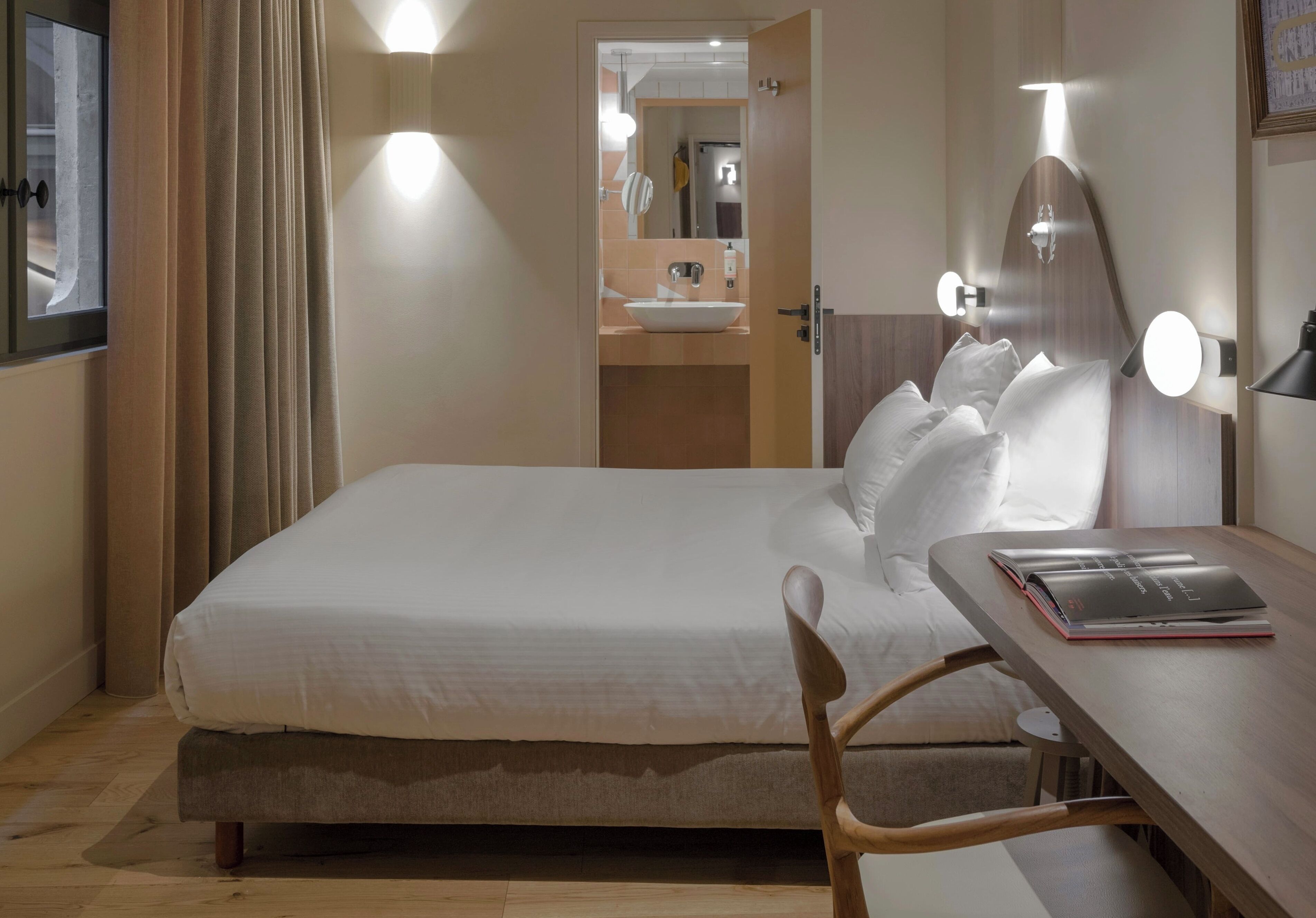 A hotel room with a bed, bedside table, and a bathroom visible through an open door.