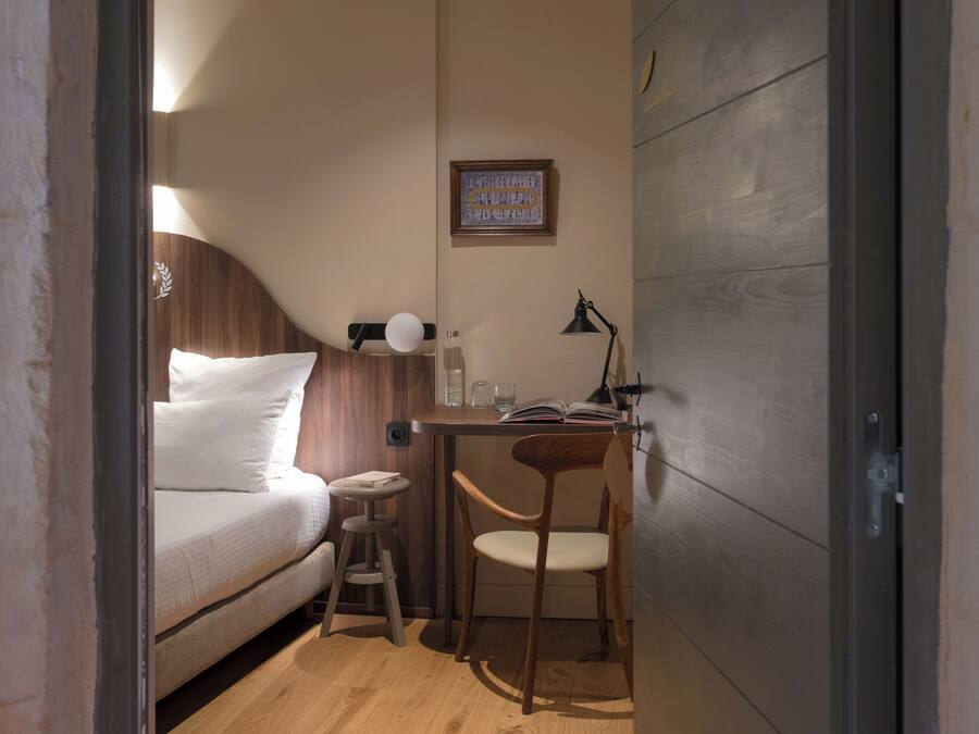 Quarto com cama, escrivaninha, cadeira e um banquinho.