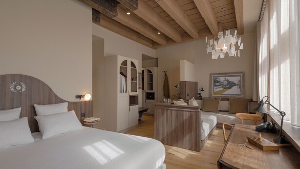 Una habitación de hotel moderna con una cama grande, vigas de madera en el techo, un escritorio con una silla y un comedor.