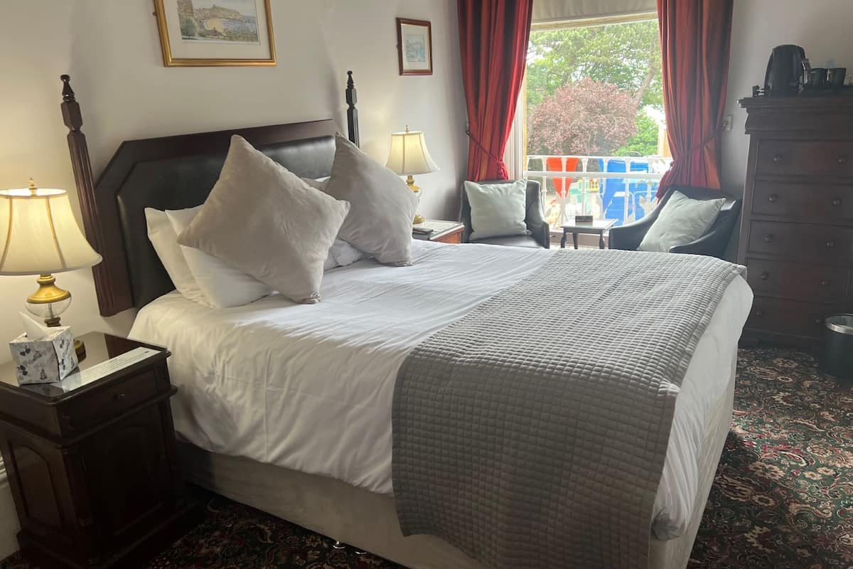 A neatly made bed with white linens and a gray quilt, a wooden nightstand with a lamp, and a dresser with a mirror.