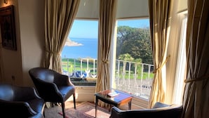 Une pièce avec vue sur la mer, comprenant deux fauteuils en cuir noir, une petite table et un tapis rouge.