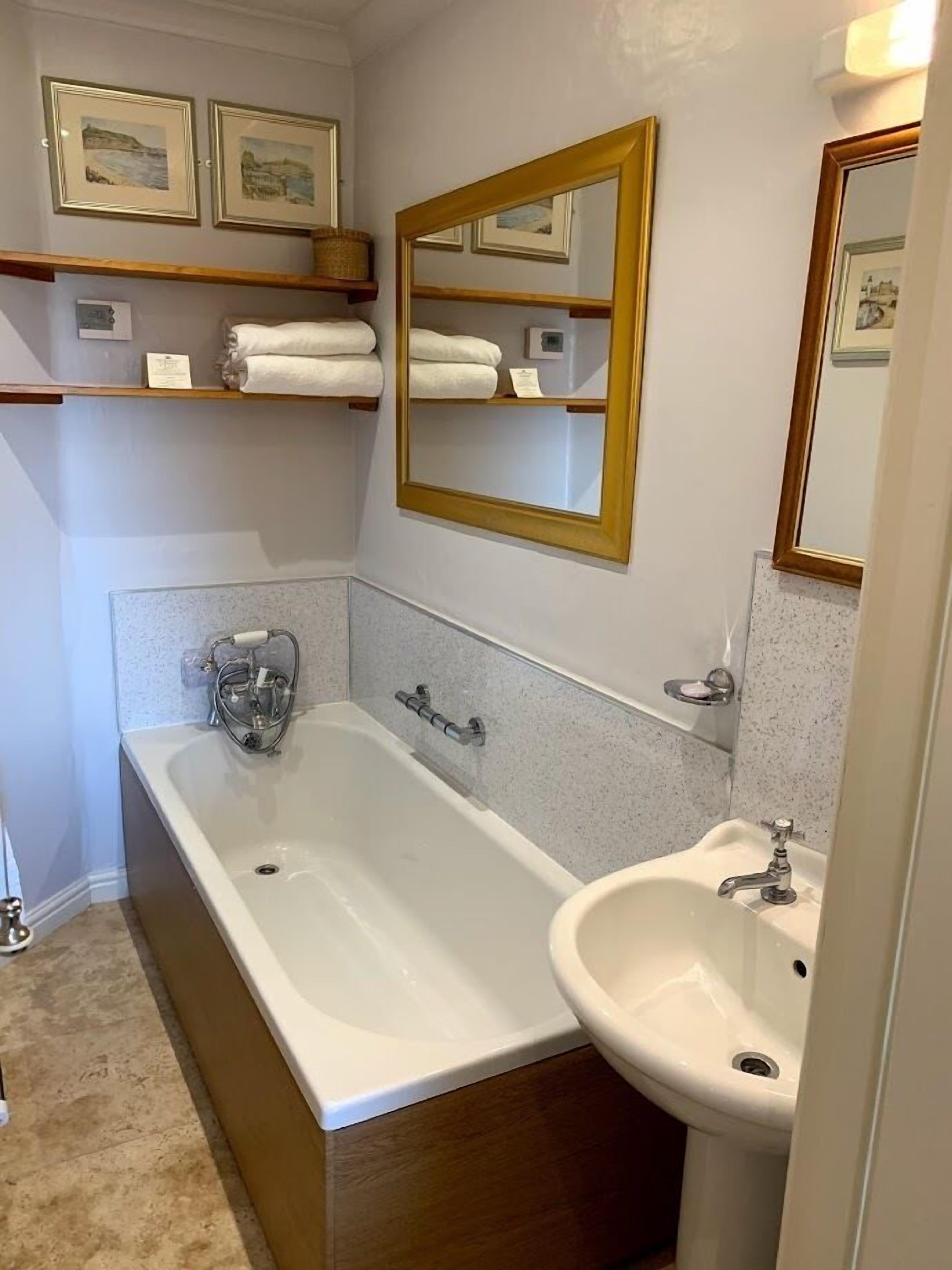 A bathroom with a bathtub, a sink, and a mirror. There are towels on a shelf above the bathtub.
