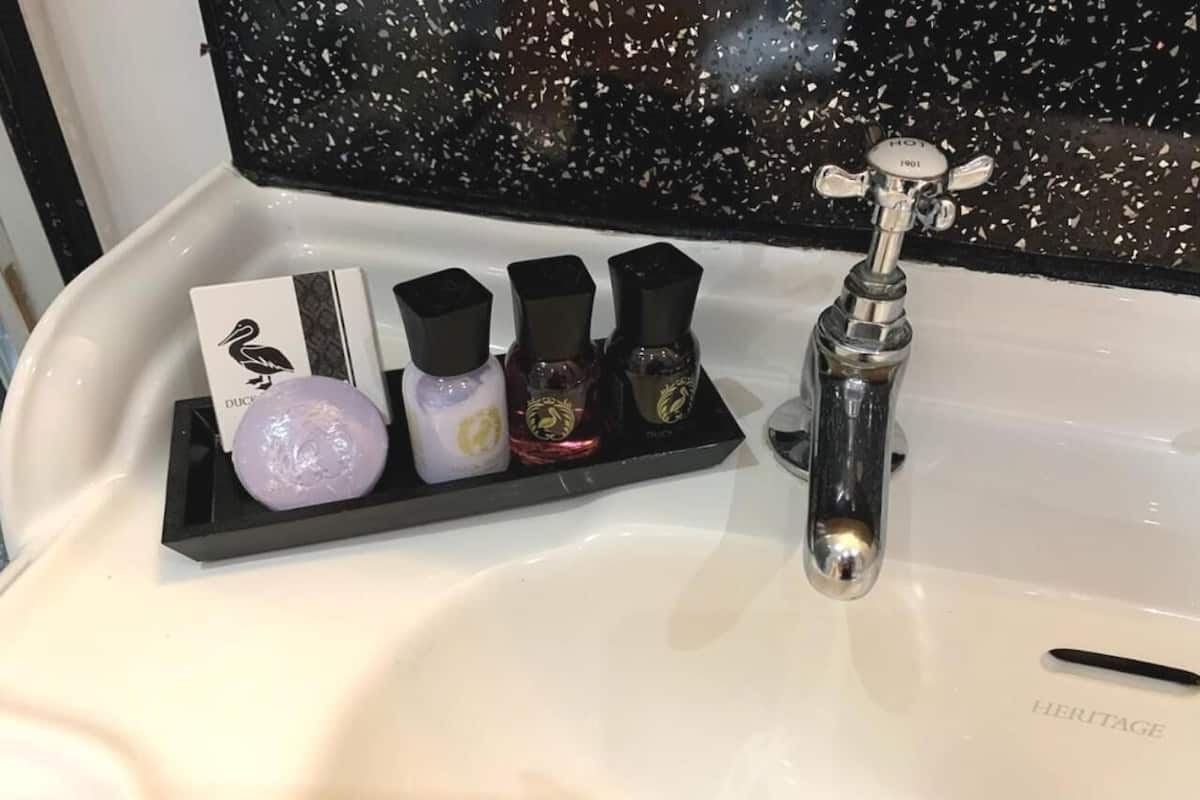 A bathroom sink with a black soap dish holding four bottles of soap and a black pen on the edge.