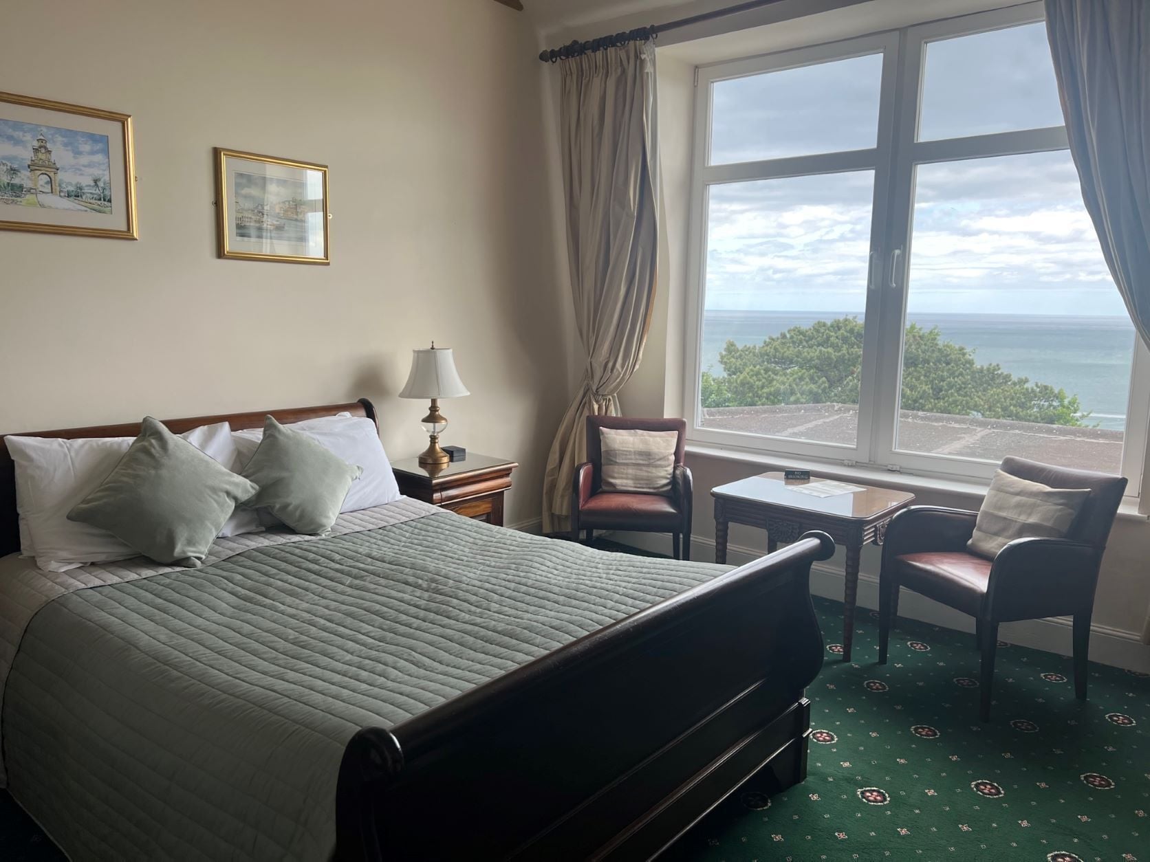 A hotel room with a bed, a chair, a small table, and a view of the ocean.