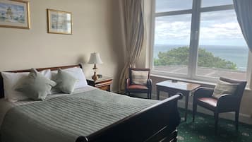 A hotel room with a bed, a chair, a small table, and a view of the ocean.