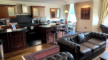 A modern kitchen with dark wood cabinets, a central island with bar stools, and a leather sofa in the living area.