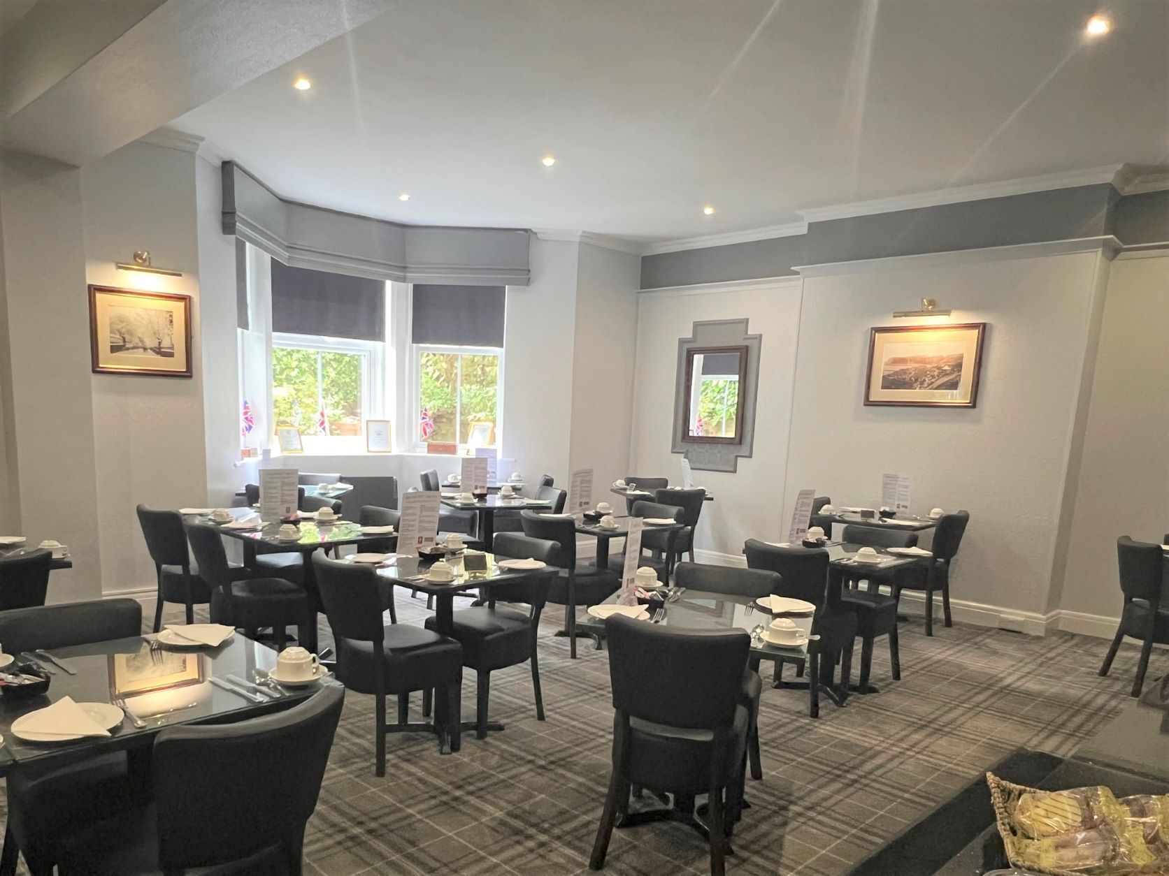 Un restaurant doté de nombreuses tables et chaises, de grandes fenêtres offrant une belle vue et de tableaux encadrés aux murs.