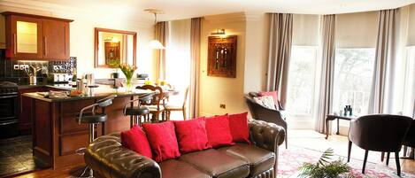 A living room with a leather sofa, a dining area, kitchen, and large windows with curtains.