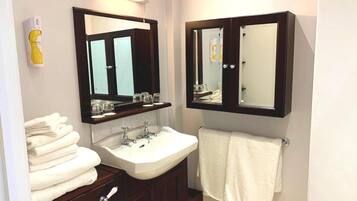 A bathroom with a white sink, two mirrors, a towel rack, and a stack of towels.