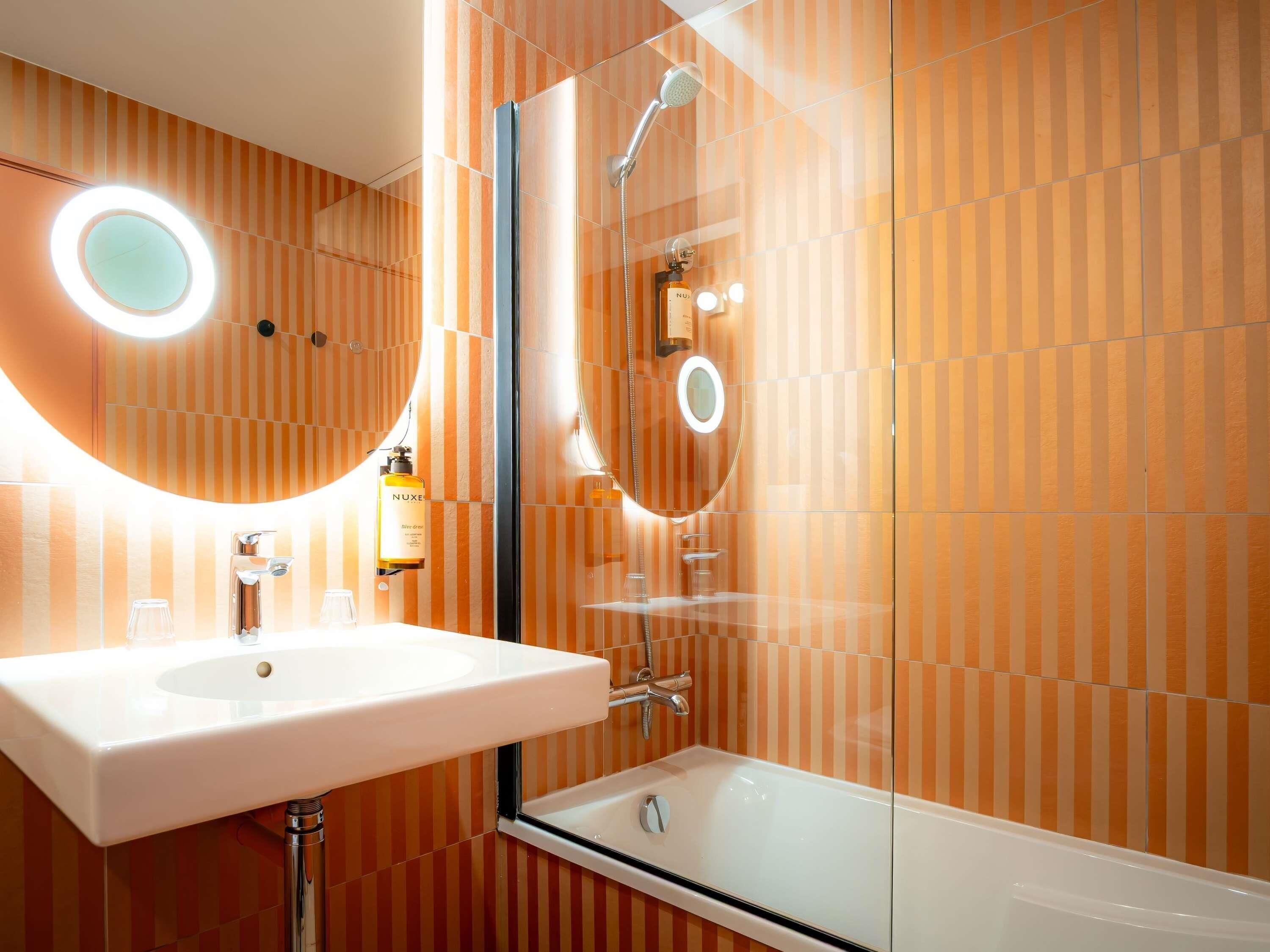 A bathroom with a white sink, a glass-enclosed shower, and striped wall tiles.