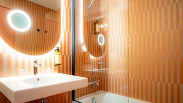 A bathroom with a white sink, a glass-enclosed shower, and striped wall tiles.