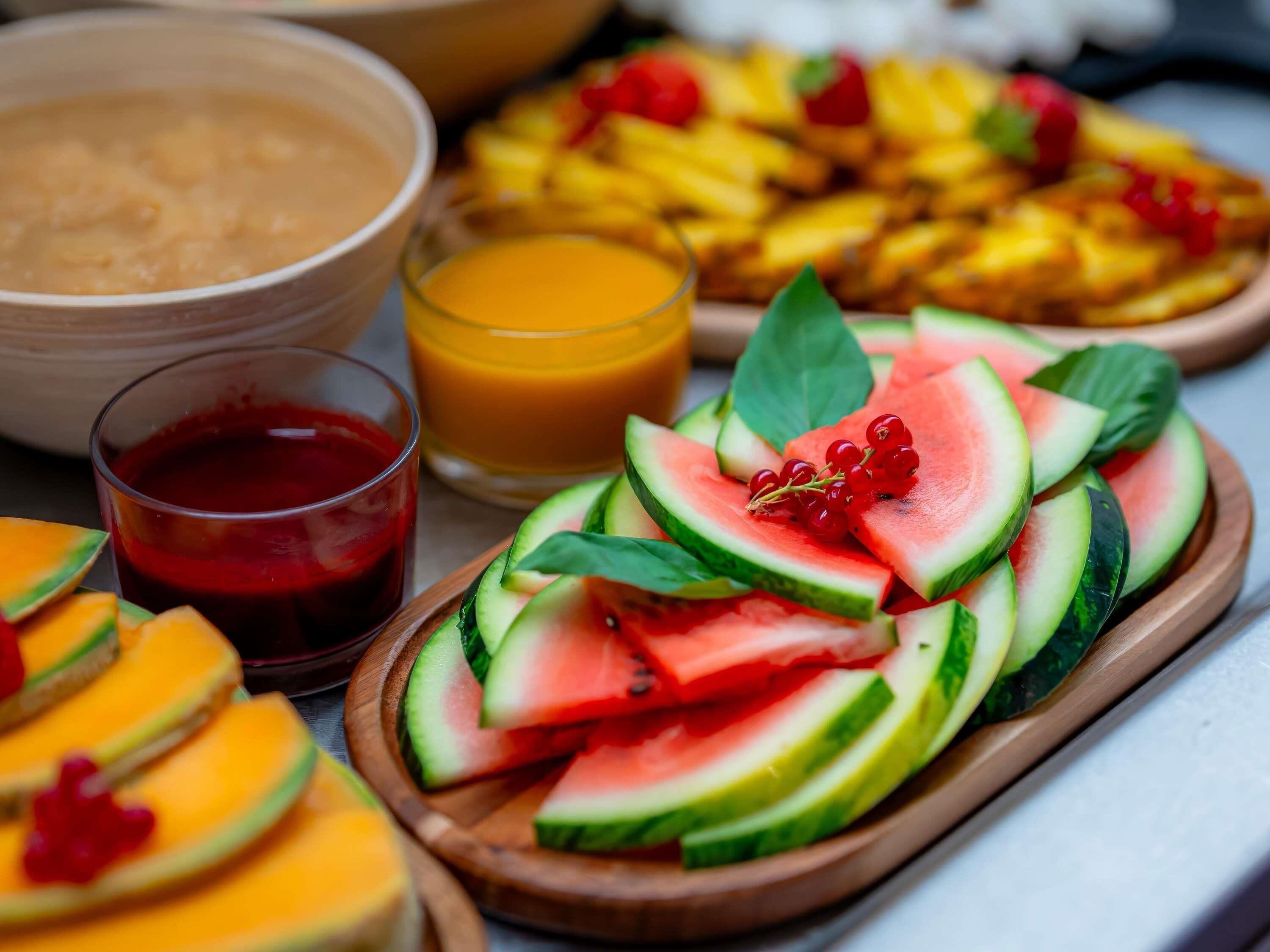 A breakfast setting with sliced fruits, a bowl of cereal, and a glass of orange juice.