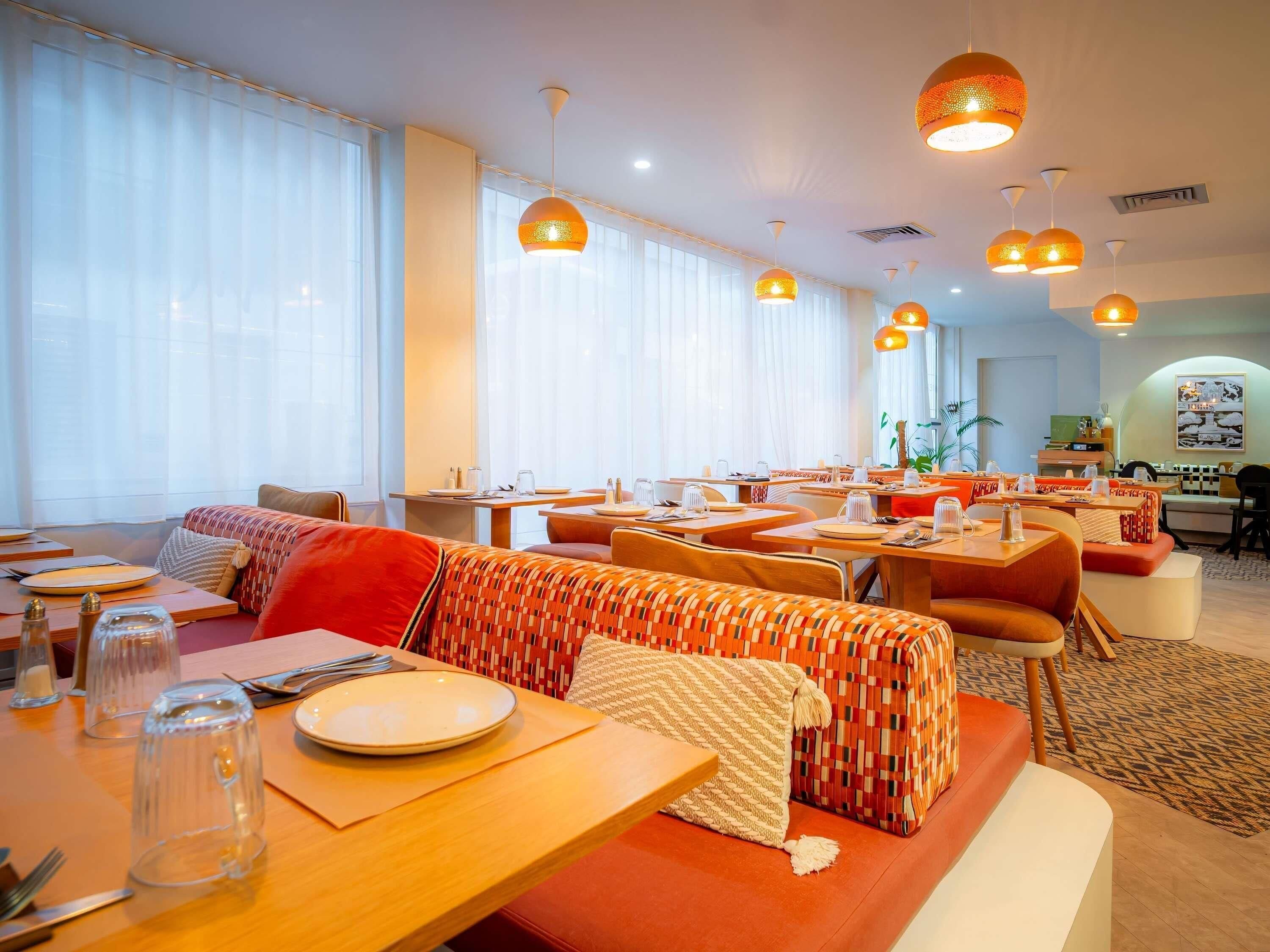 Un comedor moderno con varias mesas, bancos y lámparas colgantes.