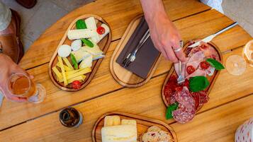 Een ronde houten tafel met diverse etenswaren, waaronder kaas, brood en vleeswaren, en een persoon die een mes en vork gebruikt.