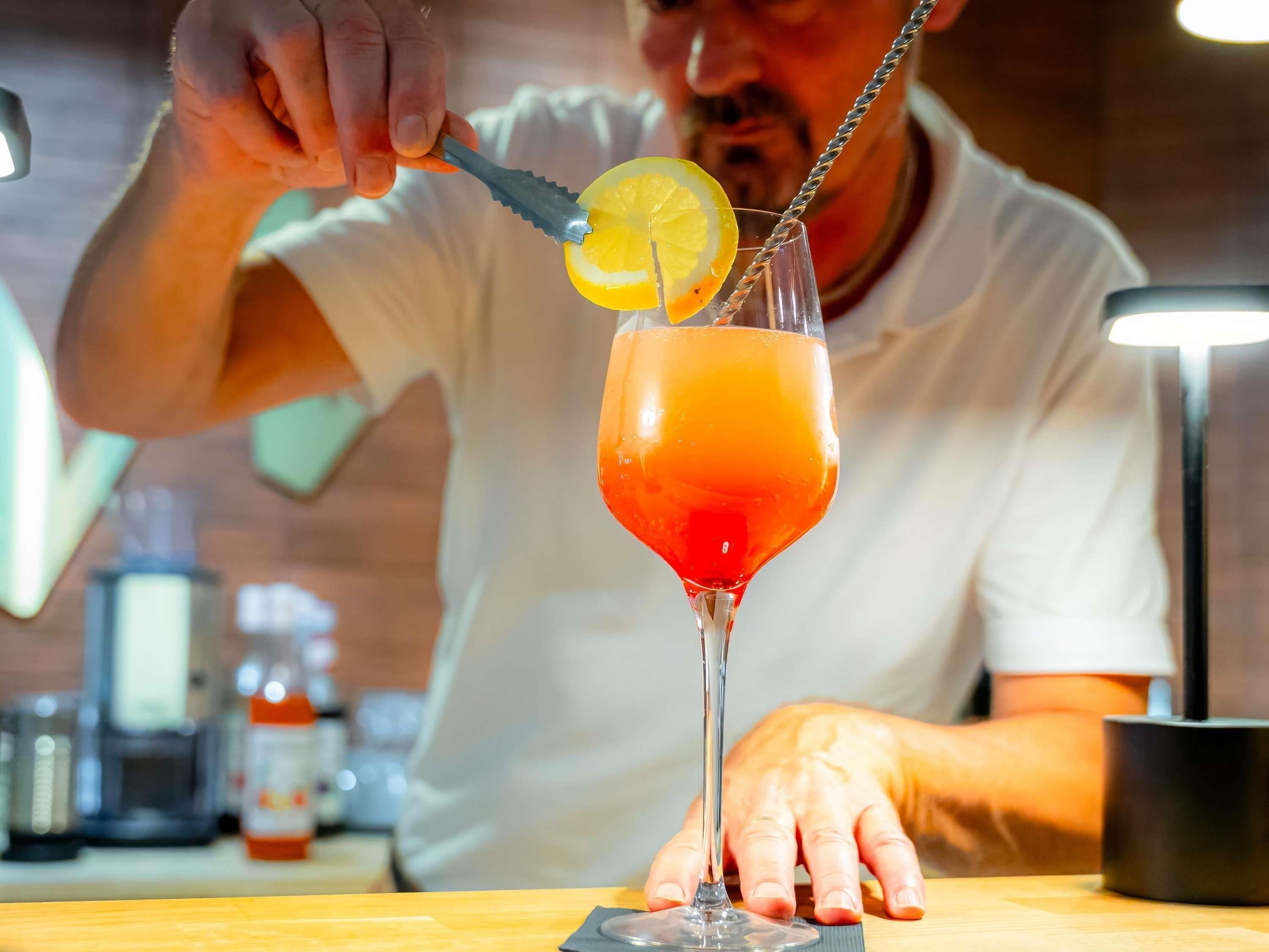 Iemand maakt een drankje met een citroenpartje als garnering in een glas.