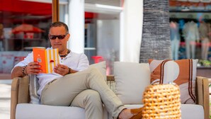 Une personne assise sur un canapé, avec un livre, un panier en osier et une petite table.