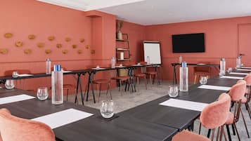Un salón de conferencias con una larga mesa, sillas, una pizarra y una pantalla.