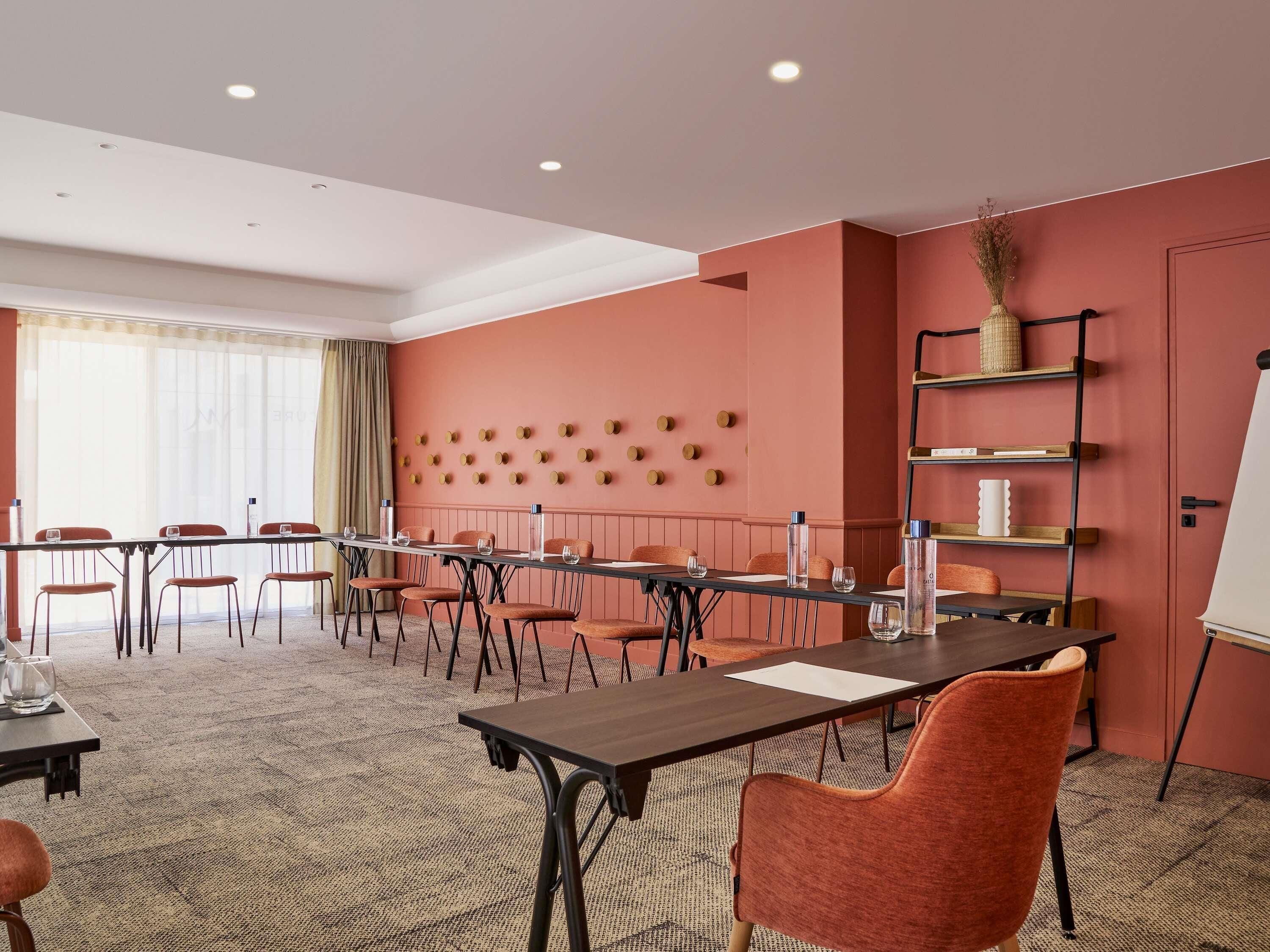 A conference room with a long table, multiple chairs, a whiteboard, and a shelving unit with decorative items.