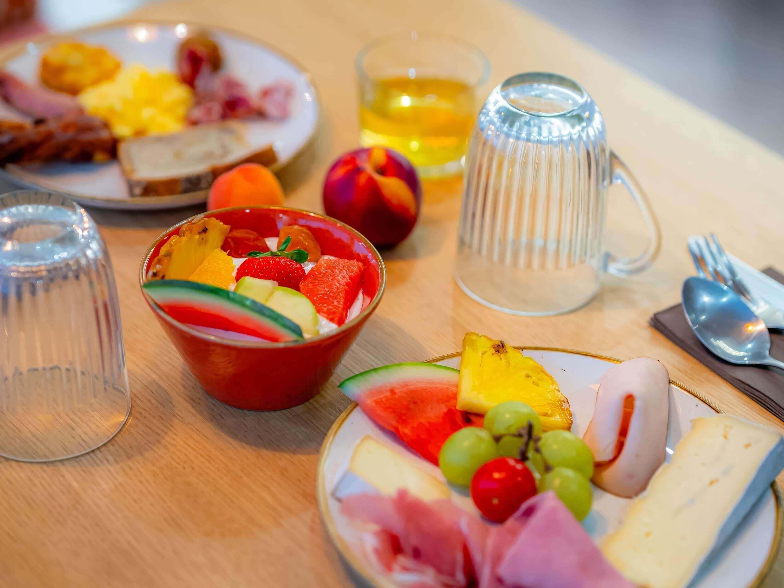 A breakfast setting with plates of food, a fruit bowl, a glass of juice, and a mug.