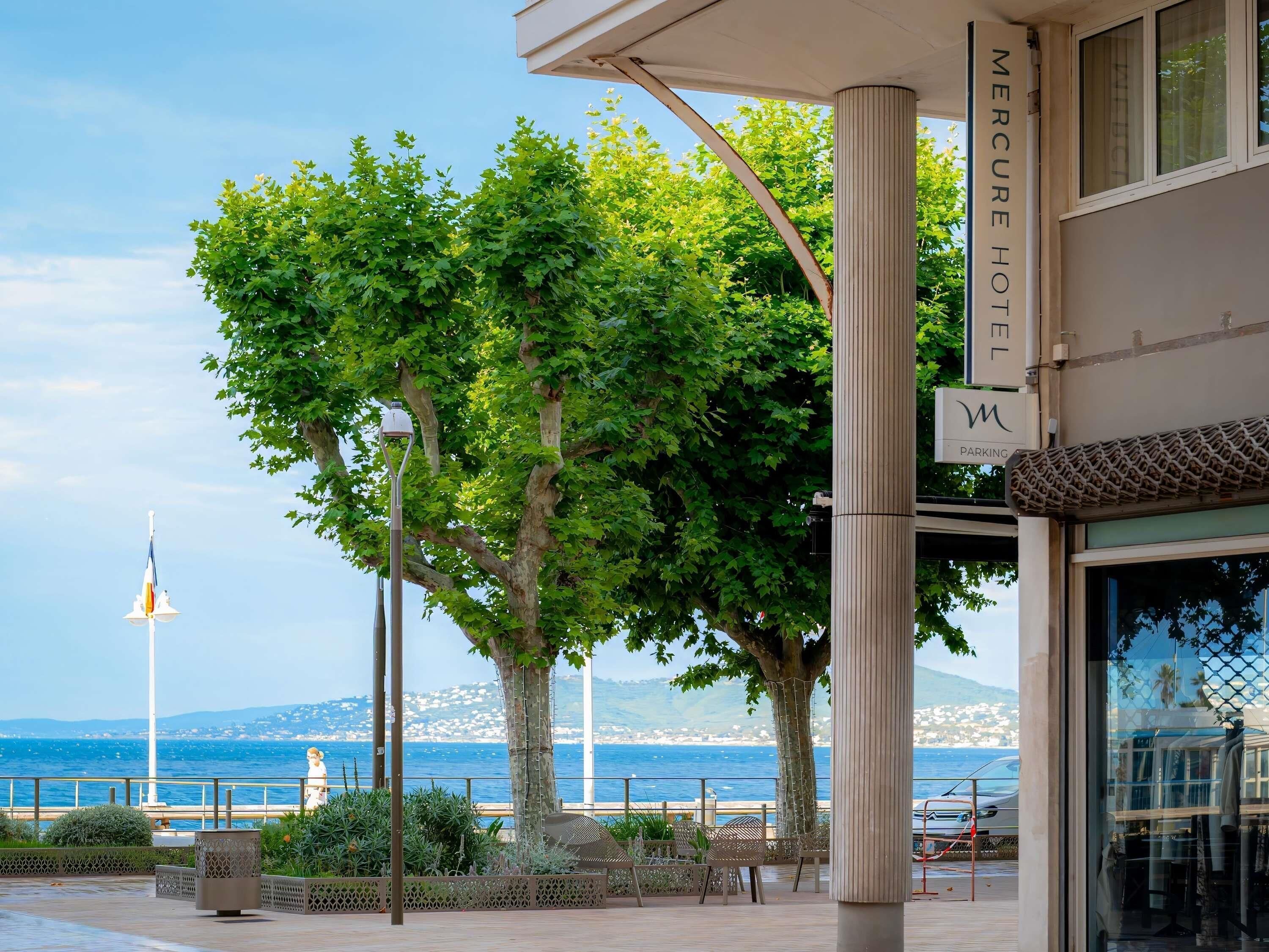 A hotel with a view of the sea, a large tree, and a street lamp.