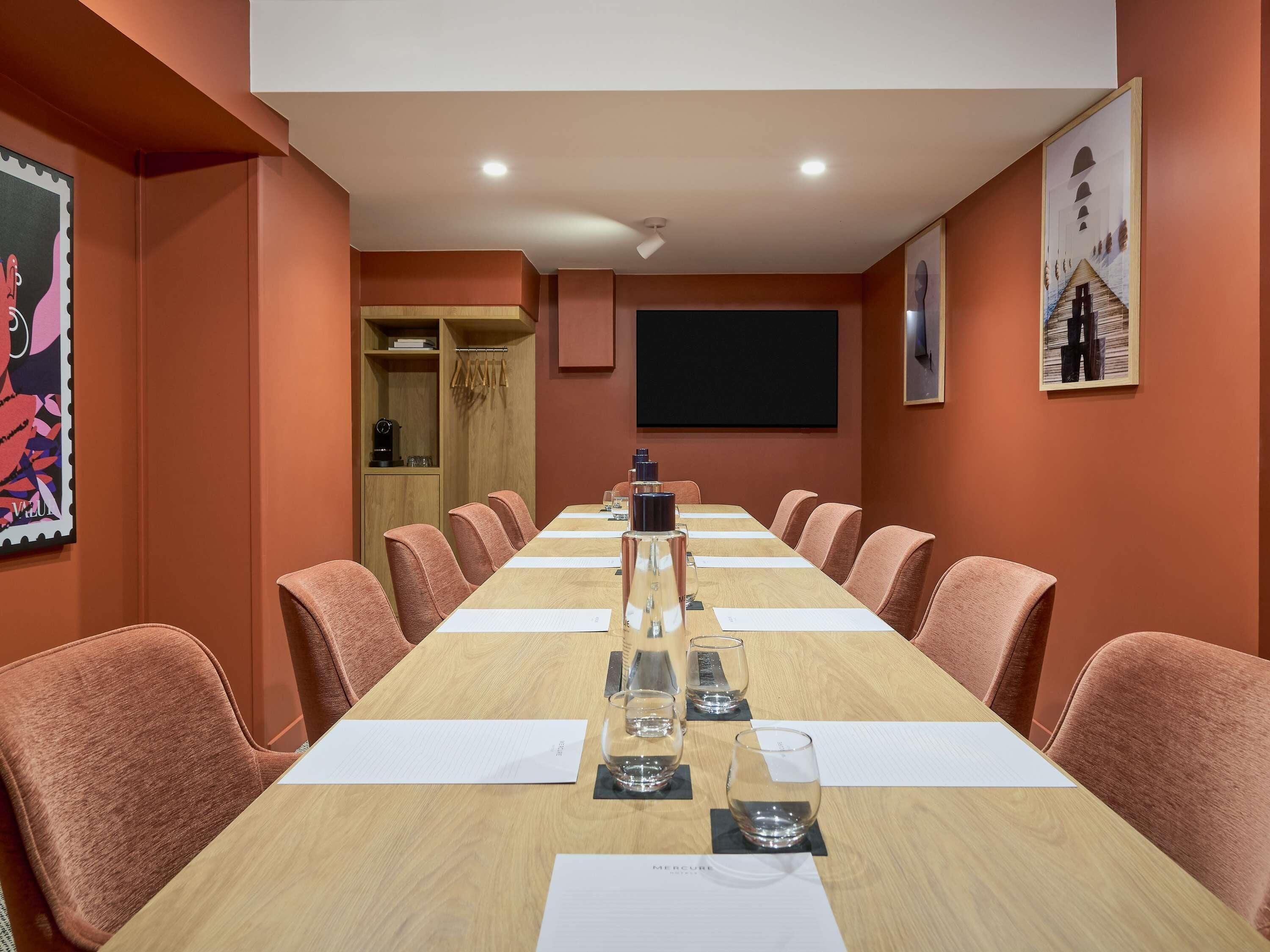 A conference room with a long table, chairs, a projector screen, and artwork on the walls.
