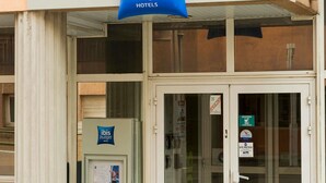 A hotel entrance with an 'ibis budget' sign, a 'Bourgoin-Jallieu' sign, and a 'Site de Protection' notice.