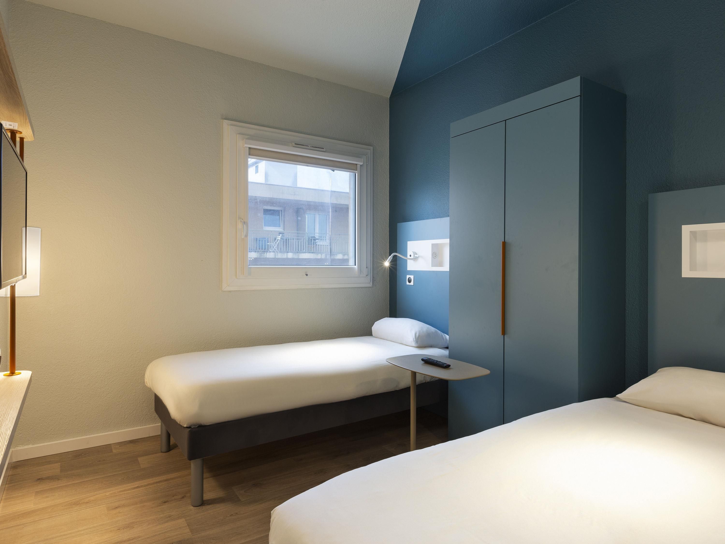 Una camera d'albergo con un letto, un tavolino, un armadio, una finestra e una lampada.