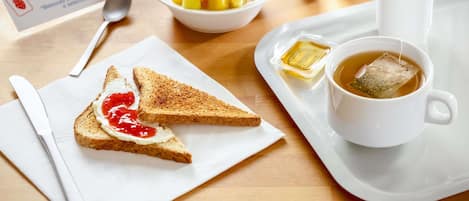 A breakfast tray with toast, jam, tea, and a bowl of fruit.