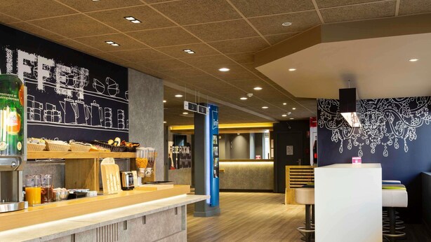 Interior de una cafetería moderna con mostrador, zona de estar y decoración en la pared.