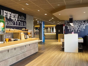 Interior de una cafetería moderna con mostrador, zona de estar y decoración en la pared.