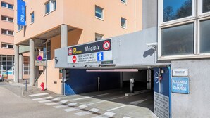 A building entrance with a sign for 'Médicis' and a parking area. - Ibis Budget Bourgoin Jallieu Centre (Bourgoin-Jallieu)