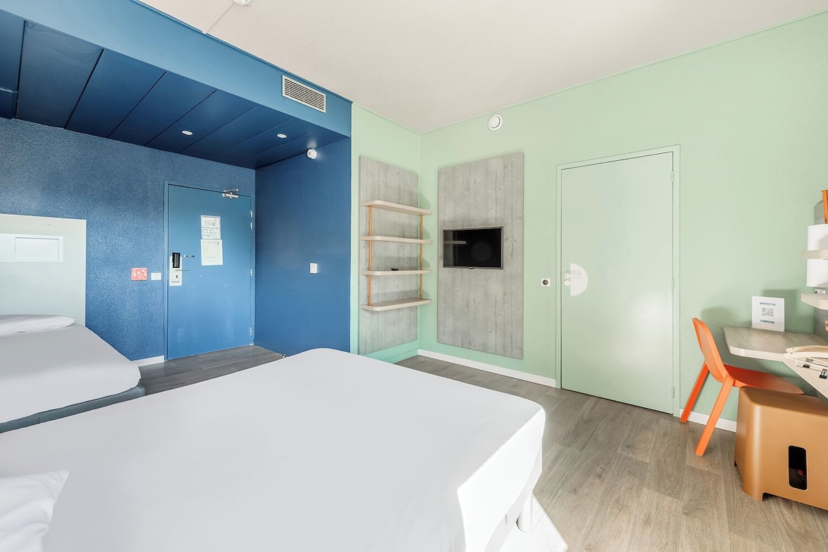 Una habitación de hotel moderna con una cama grande, un escritorio con una silla y un televisor montado en la pared.