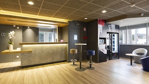 Una zona de recepción moderna con un mostrador de madera, dos taburetes y un área de estar con una silla azul.