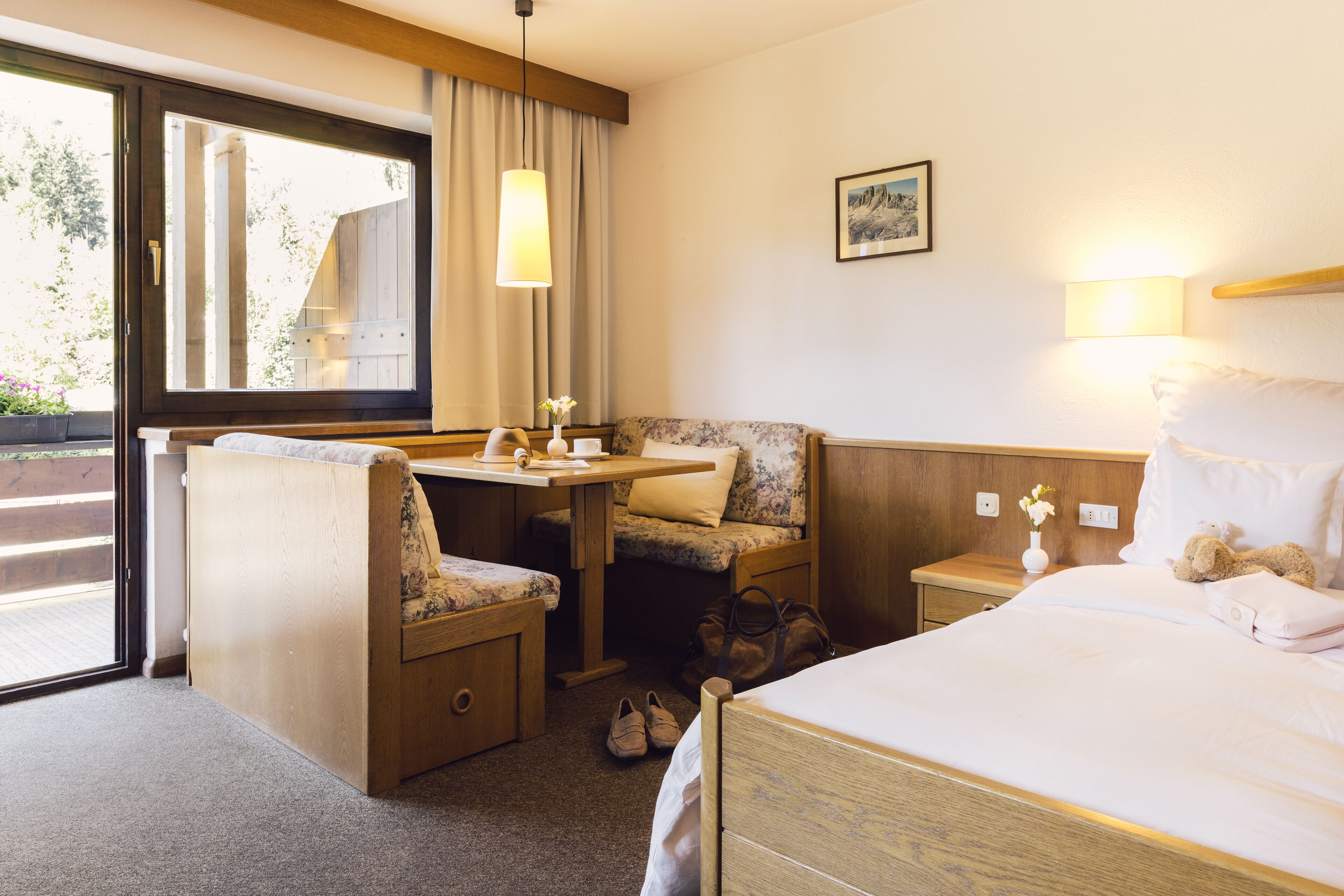 Una camera d'albergo con un letto, una scrivania con una sedia, un tavolino, un comodino e una finestra con tende.
