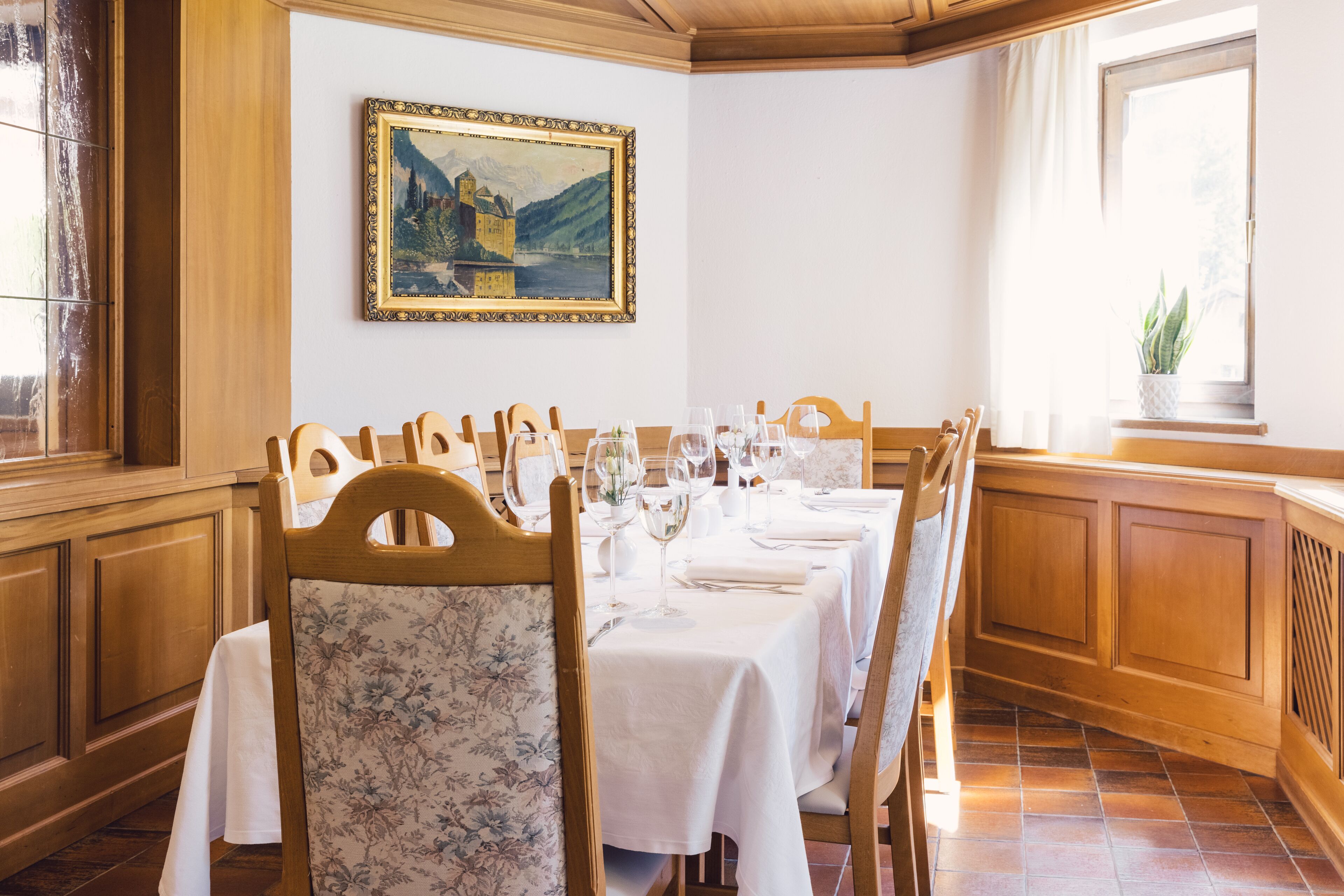 Un comedor con sillas y mesas de madera, un cuadro en la pared y una ventana con una planta.