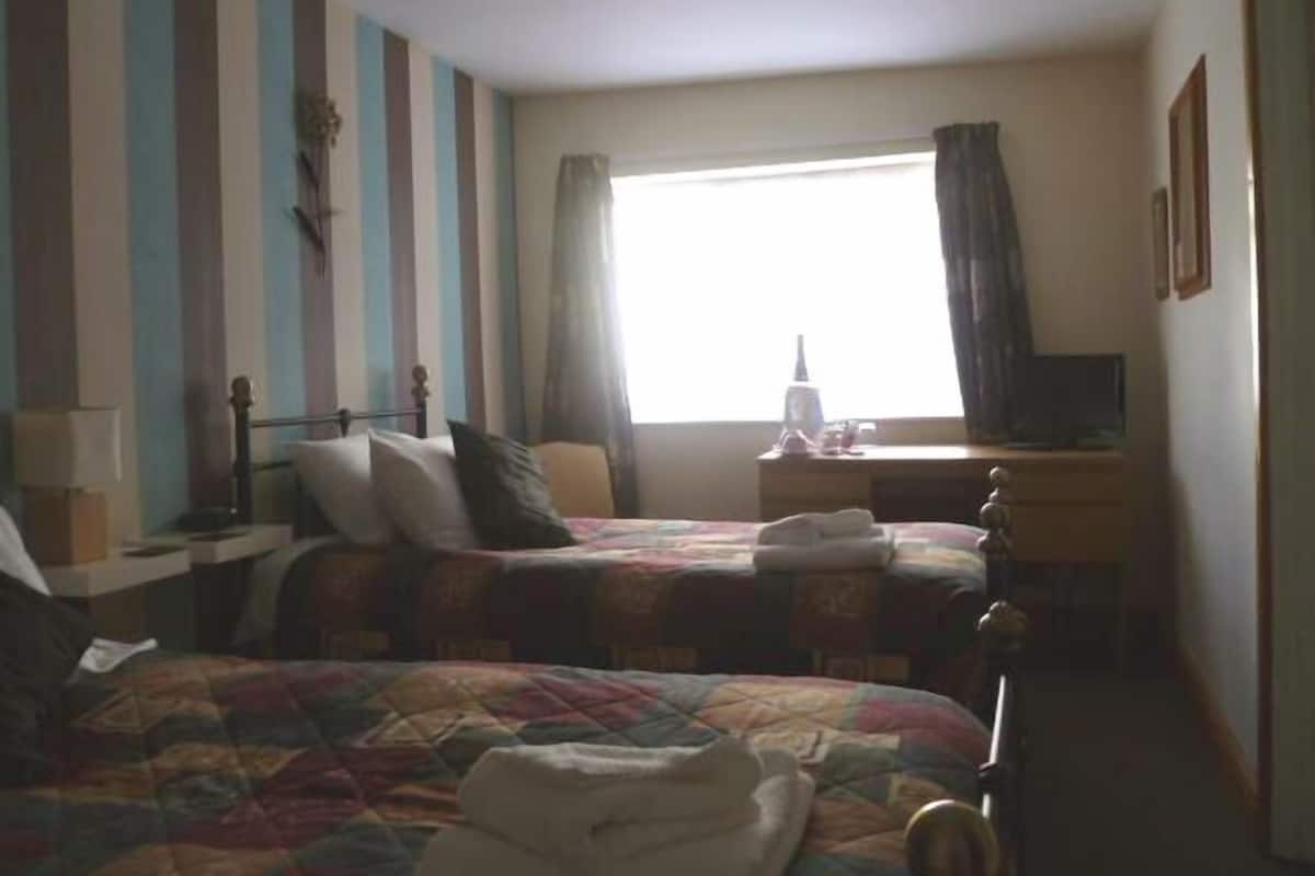 Une chambre d’hôtel avec deux lits, un bureau, une chaise et une fenêtre avec des rideaux.