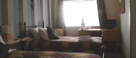 A hotel room with two beds, a desk, a chair, and a window with curtains.
