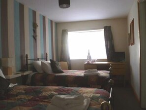 A hotel room with two beds, a desk, a chair, and a window with curtains. - Belle Vue Hotel (Llanwrtyd Wells)