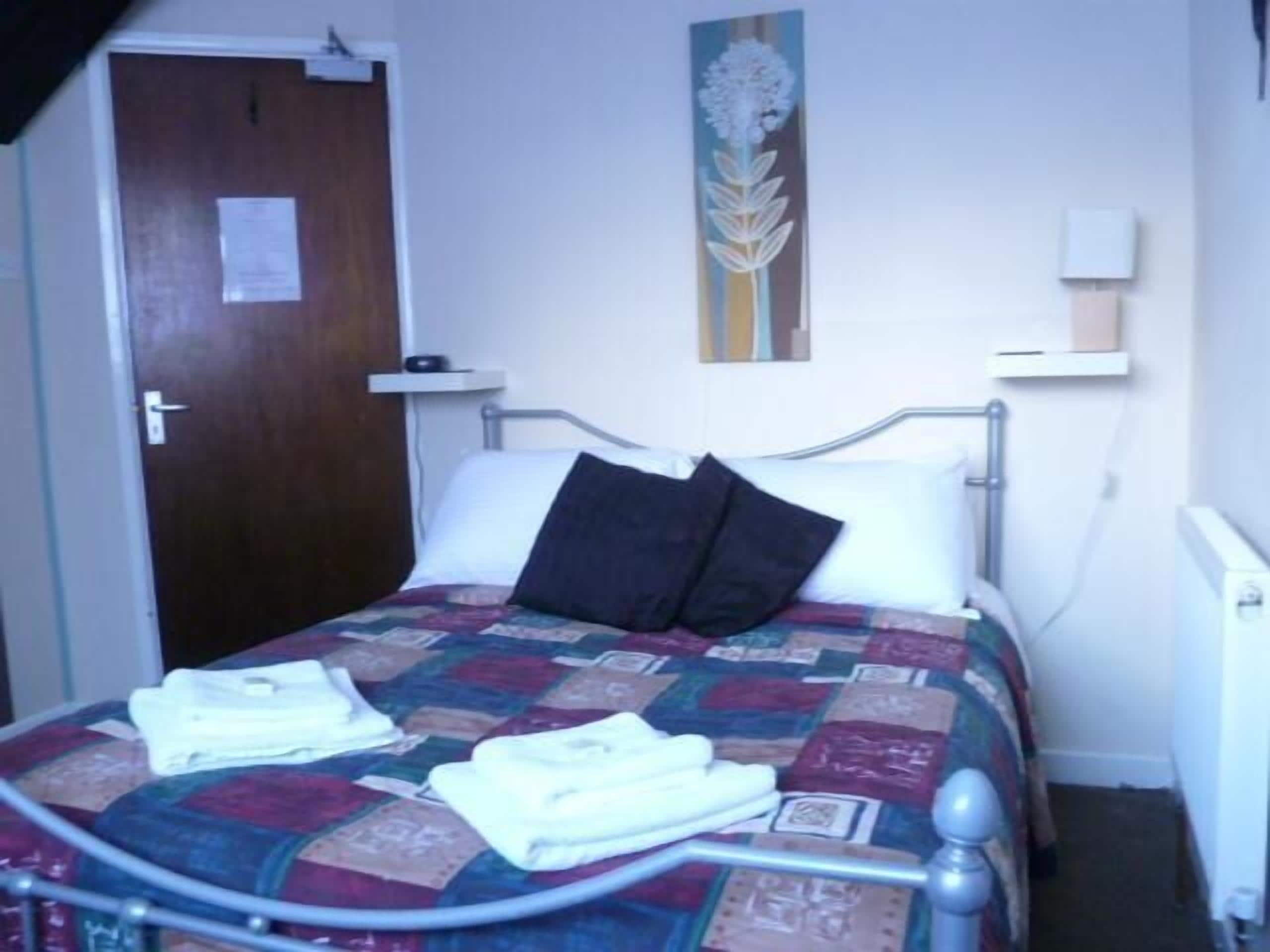 Un lit simple avec un cadre en métal, une couette, deux oreillers et une table de chevet avec une lampe.