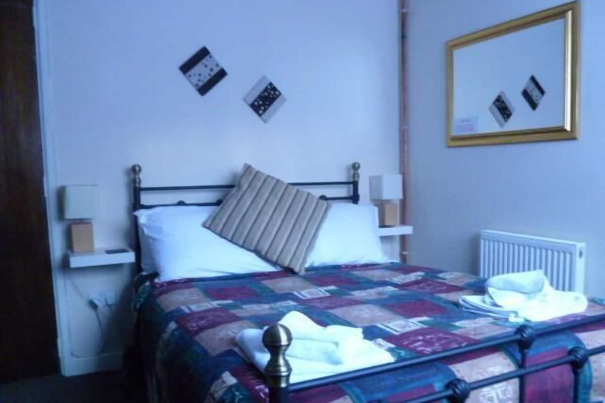 Un lit bien fait, avec une couverture matelassée, une lampe de chevet et un miroir fixé au mur.