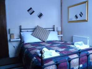 A neatly made bed with a quilt, a bedside lamp, and a wall-mounted mirror. - Belle Vue Hotel (Llanwrtyd Wells)