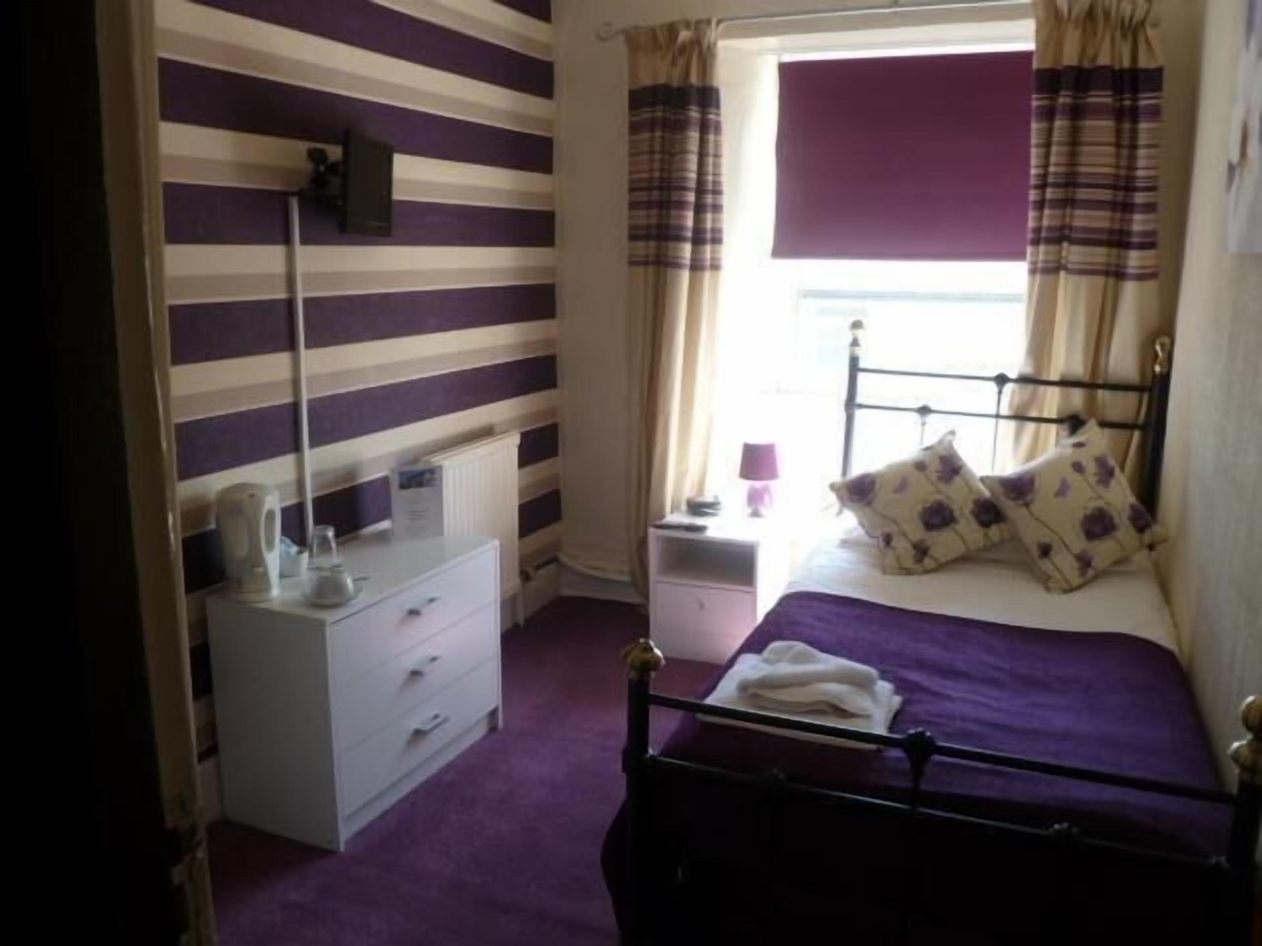 A bedroom with a bed, a bedside table, a lamp, and a window with curtains.