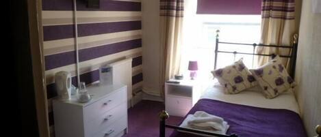 A bedroom with a bed, a bedside table, a lamp, and a window with curtains.